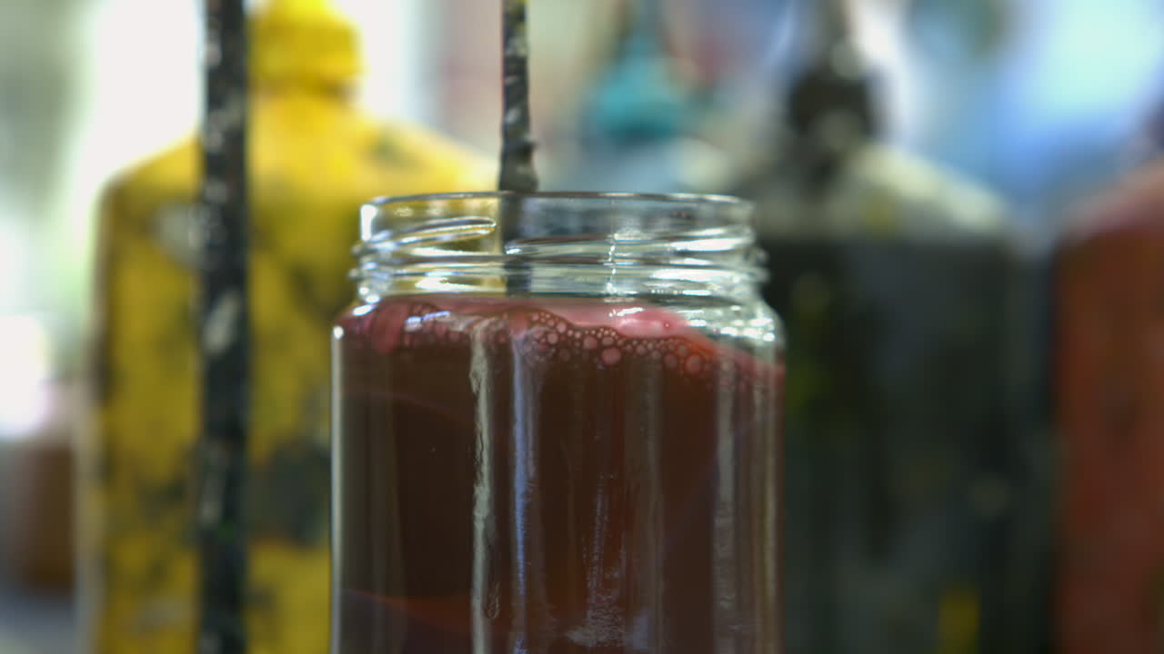 Extreme closeup of glass jar filled with mixed paint being stired by a mechanical whisk