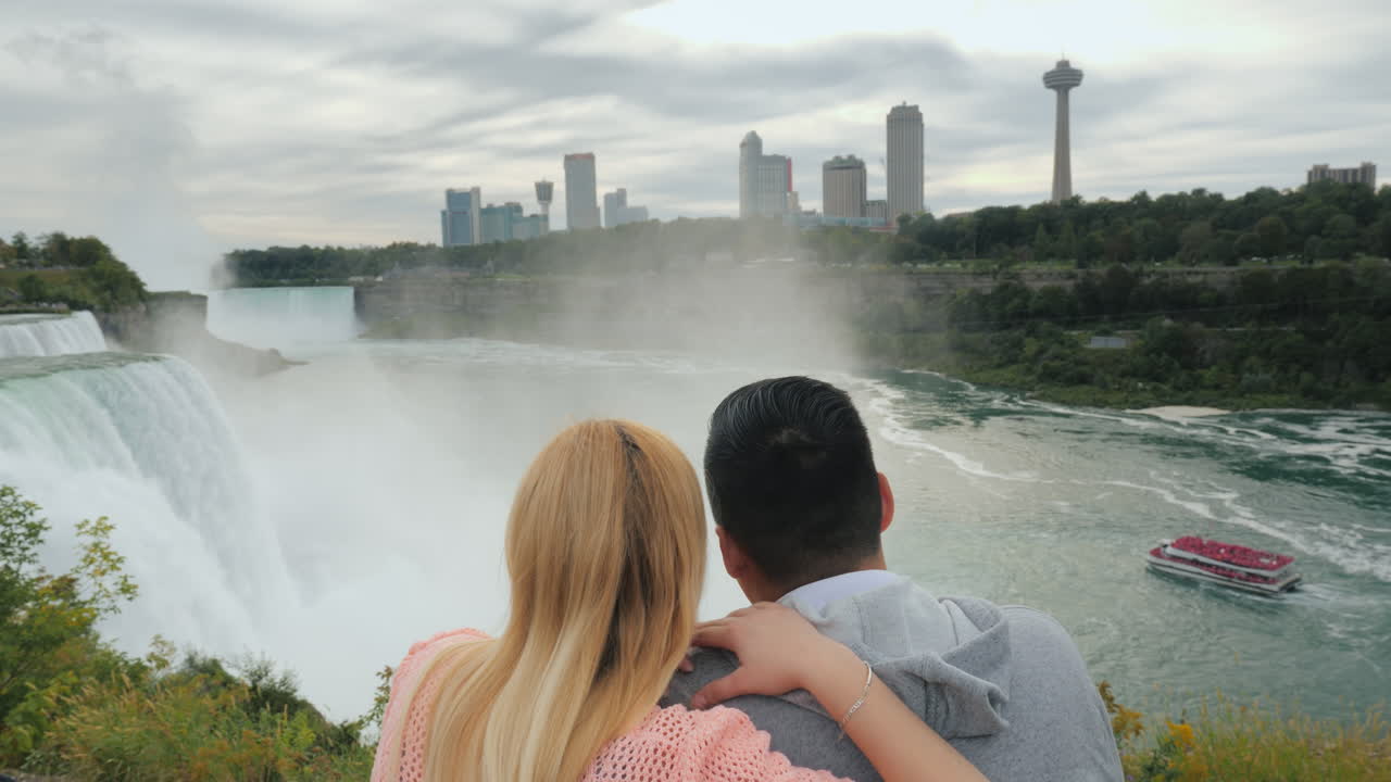 나이아가라 폭포 전망대에서 다민족 커플이 포옹하며 디를 바라보고 있습니다.