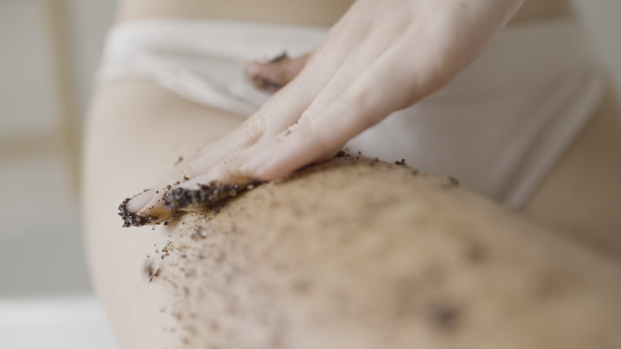 Woman applying coffee scrub to leg