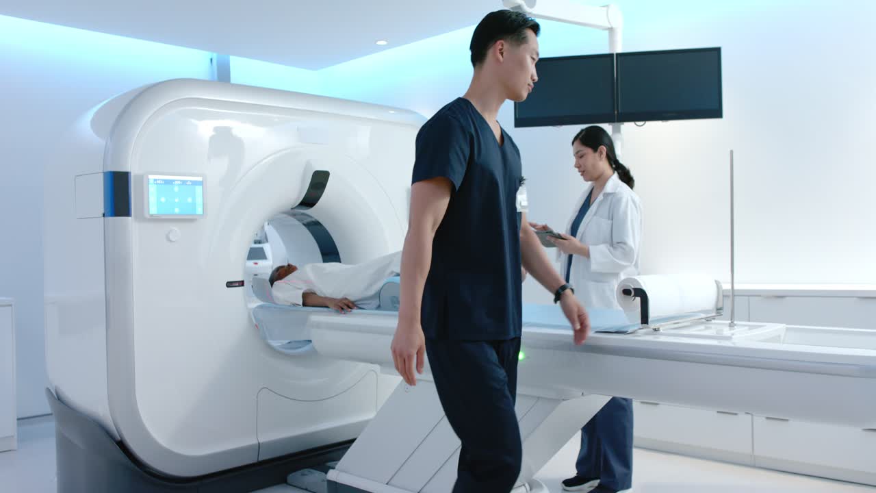 Team della risonanza magnetica che controlla la posizione del paziente africano, il tecnico che sistema il cuscinetto, il paziente che viene introdotto nel tunnel, il medico che controlla il tablet.