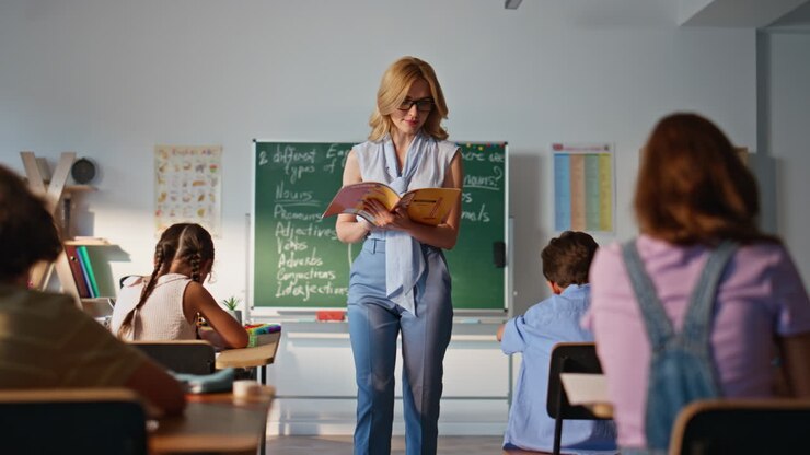 Tutor reading task classroom from book. Young woman teacher talking pupils