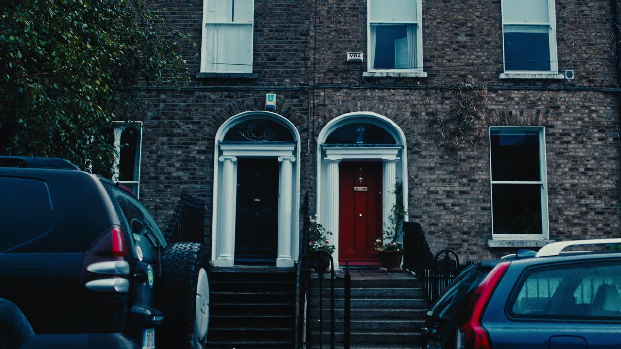 A shot of traditional Irish houses with bordeaux and brown doors, brick walls, windows, columns, and stairs leading to the entrance - Ireland