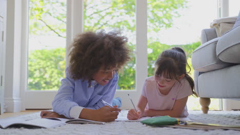 boy and girl lying on rug in lounge at home doing school homework together