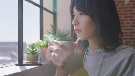 beautiful young asian woman drinking coffee at home enjoying relaxed morning looking out window planning ahead thinking contemplative female in trendy apartment