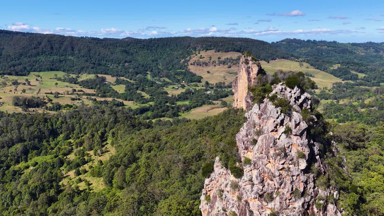 Drone footage captures Nimbin Rocks surrounded by vibrant greenery under clear skies, showcasing the natural beauty of New South Wales