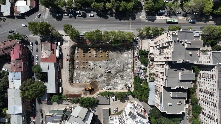 Uma vista aérea de um terreno escavado cercado por edifícios da cidade, pronto para a construção de um novo projeto