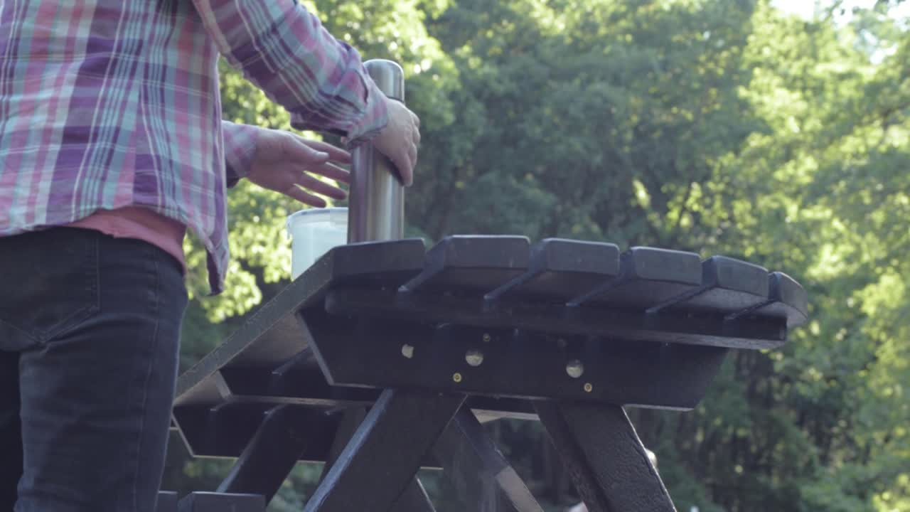Woman pouring drink from flask at wooden picnic table low medium shot