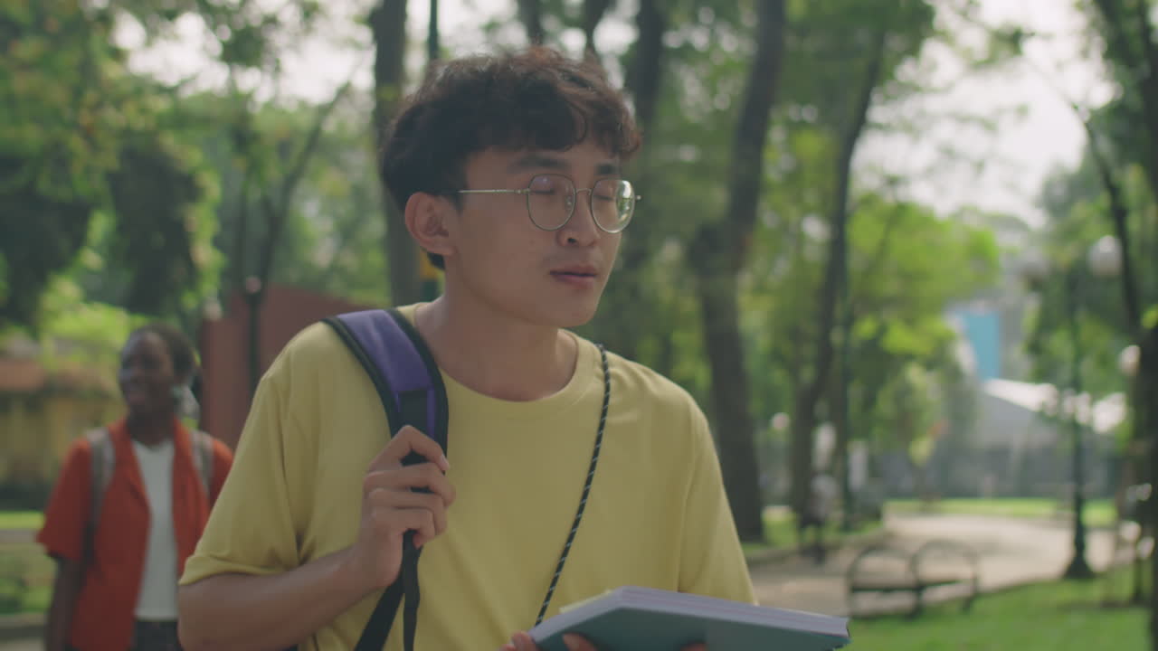 Asian College Student Walking in Park with Workbook