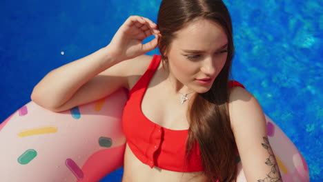 tattooed girl in red swimsuit on the swimming circle in the pool. brunette enjoying the sun at leisure time in summer.