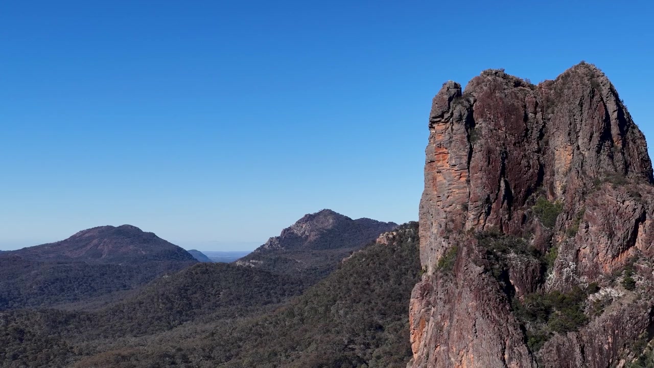 Toma panorámica estática de una aguja de roca volcánica bajo un cielo azul claro en el Parque Nacional Warrumbungle