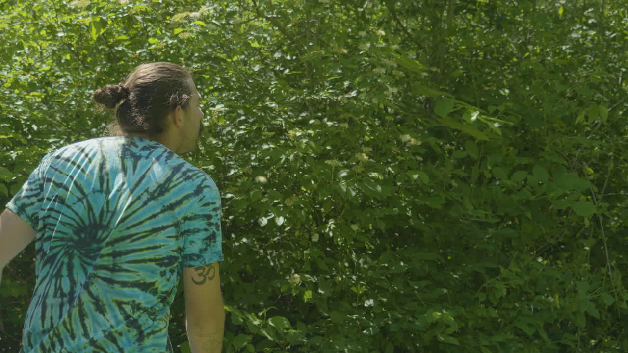 un hombre completa su lanzamiento de disco de golf con un movimiento de seguimiento contra un telón de fondo de densa vegetación, mostrando la naturaleza dinámica del deporte