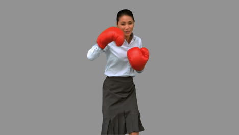 mujer de negocios con guantes de boxeo y golpeando en la pantalla gris