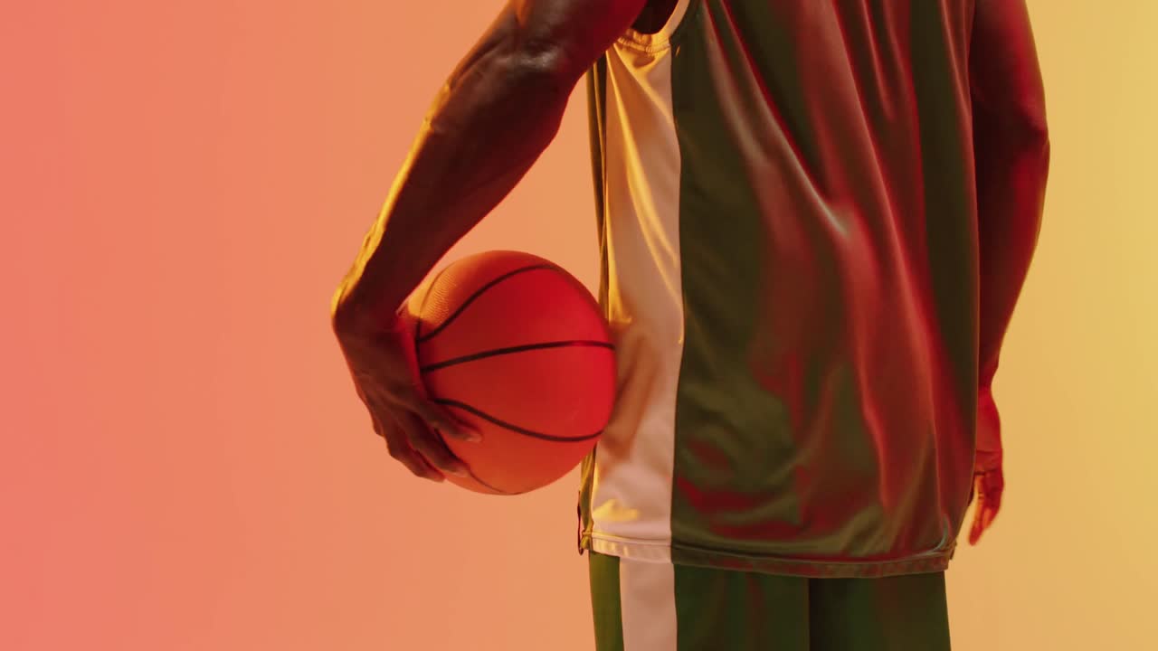 video de la vista trasera de un jugador de baloncesto afroamericano sosteniendo la pelota sobre un fondo naranja.