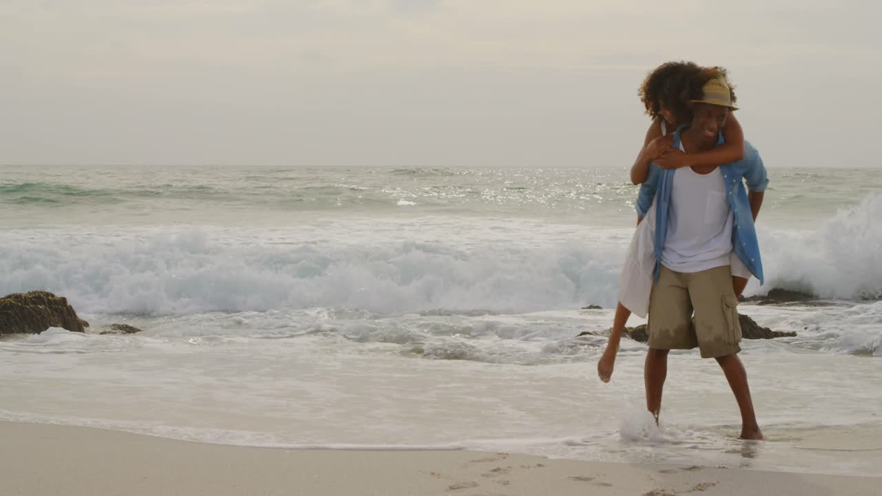 African american man giving piggyback ride to woman on the beach 4k