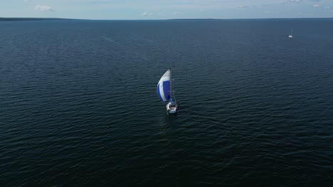 un velero navega con gracia por el mar báltico con una colorida vela gennaker, vista desde atrás, perspectiva de avión no tripulado, algunas islas en el horizonte