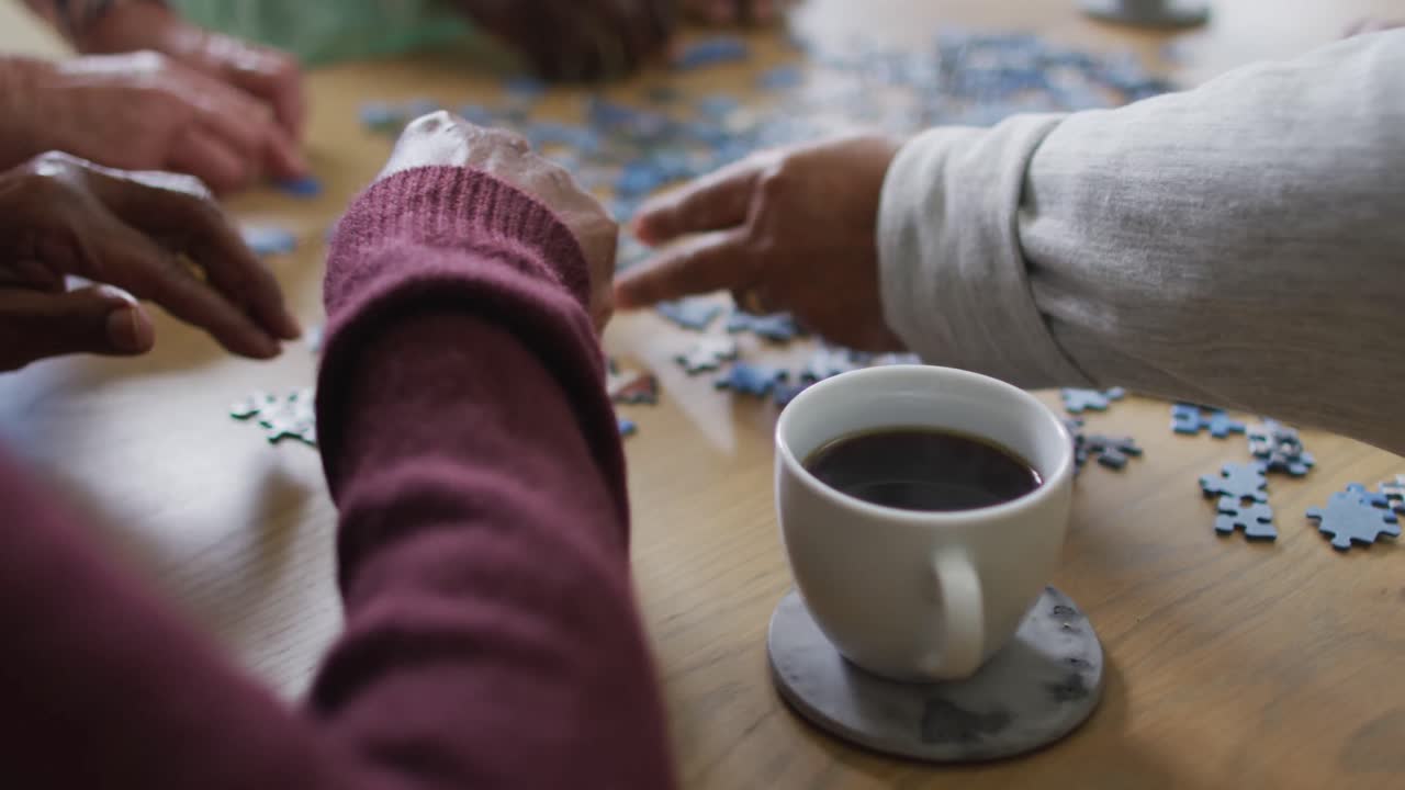 Mani di un gruppo di amici anziani e diversi che bevono caffè e fanno un puzzle a casa.