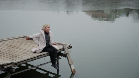 woman sitting on a wooden pier by a frozen lake