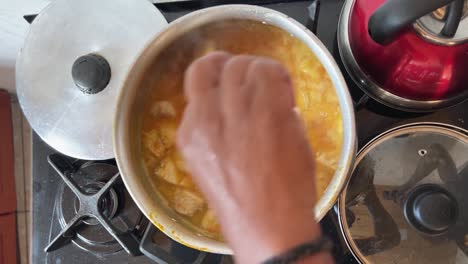 hand stirring a large metal pot of delicious tropical brazilian fish stew with a wooden spatula on a gas stove in the state of rio grande do norte in northeastern brazil