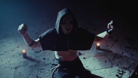 man in dark hood in ritualistic pose