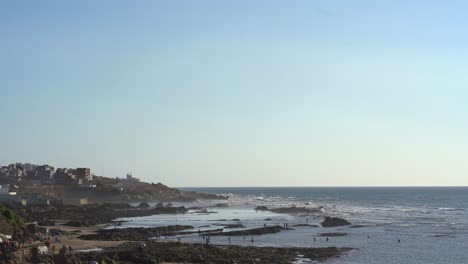 Static-aerial-footage-of-Asilah-city,-Morocco,-showing-tourists-and-locals-on-the-beach