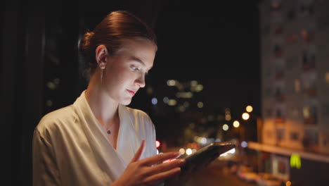 Woman using tablet at night with city lights in the background