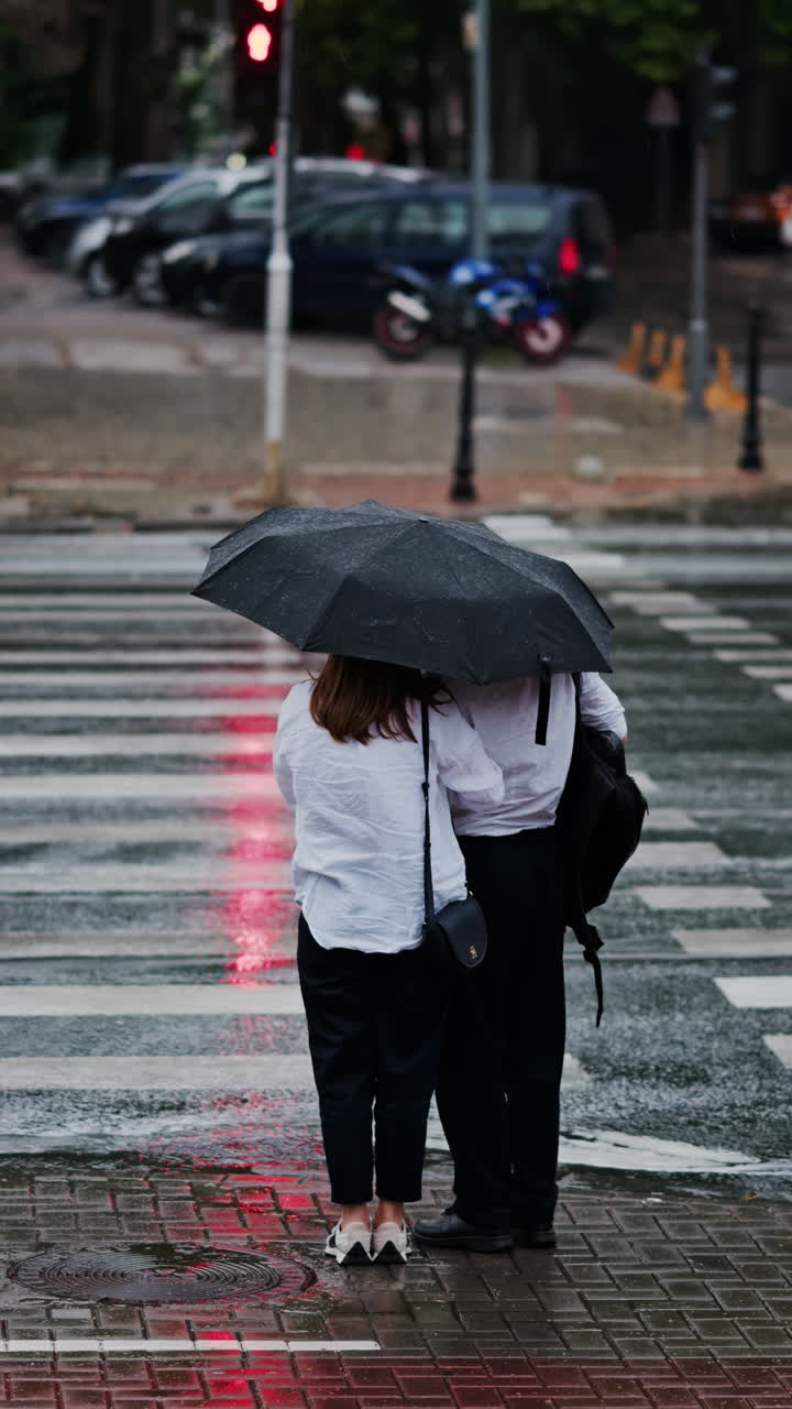 Two girls holding an umbrella waiting at a pedestrian crossing on a rainy day in Chisinau, Moldova. Vertical