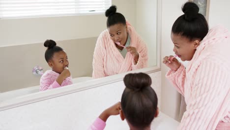 Happy-unaltered-african-american-mother-and-daughter-brushing-teeth-in-bathroom,-in-slow-motion