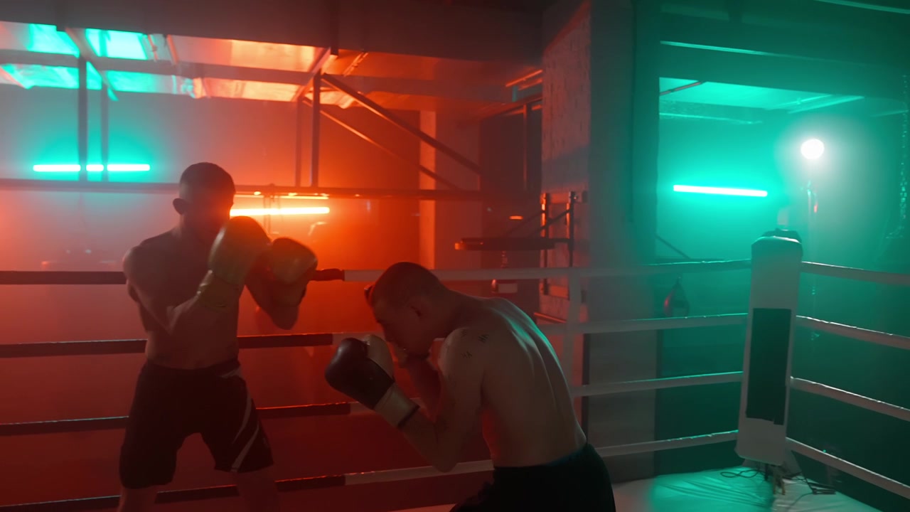 Due pugili che si allenano e fanno shadow boxing in un ring da palestra illuminato al neon.
