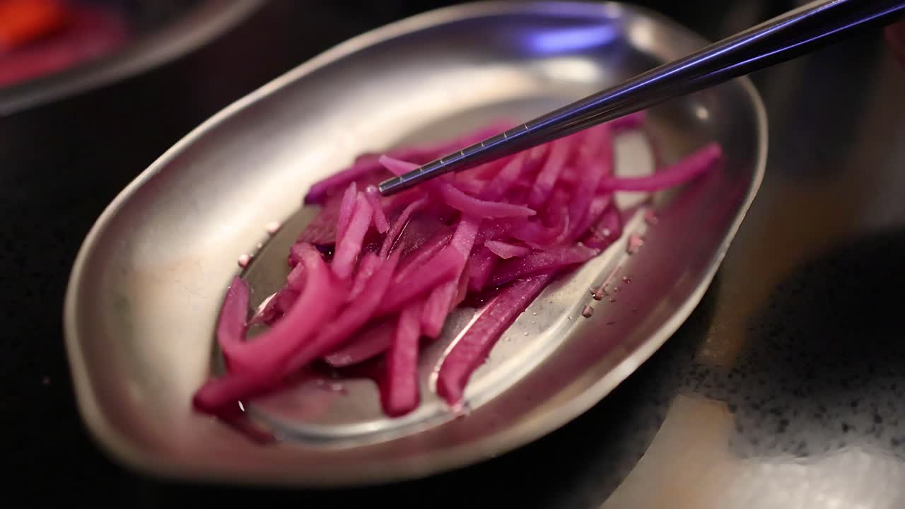 Chopsticks picking up pickled red onions from dish