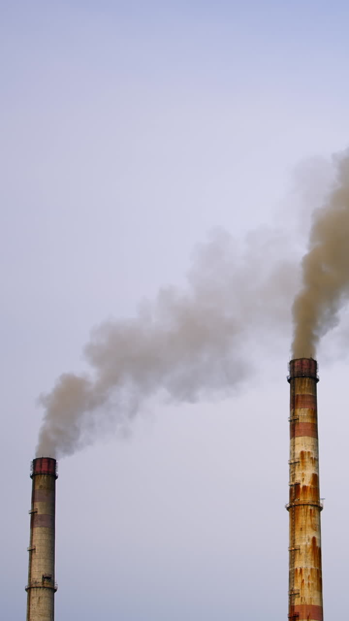 Factory pipes with smoke. Dirty smoke pours out of chimneys into the air on the river background. Aerial view video. Vertical video