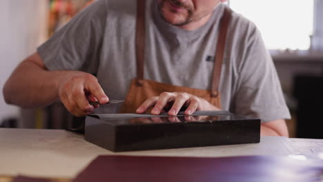 Artesano-Afila-El-Cortador-Con-Papel-De-Lija-En-La-Mesa-De-La-Tienda