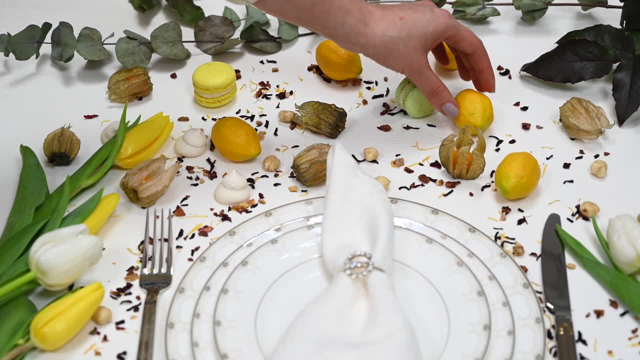 Close up of a nicely folded napkin on a plate on a set table wit flowers, macarons and lemons as decorations