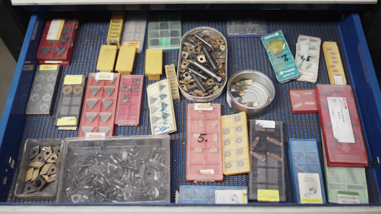 Shot an organized workshop drawer containing various carbide cutting inserts, metal bits, and small tools