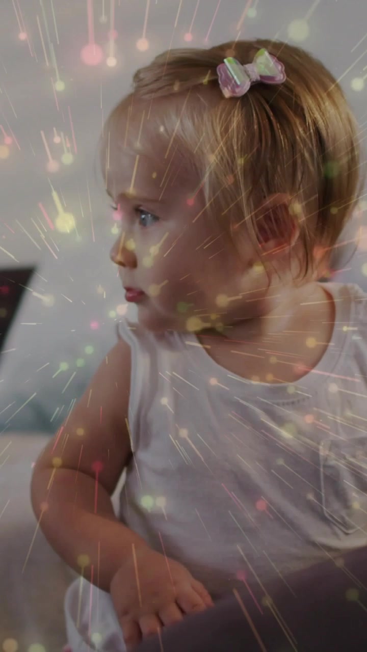 Video verticale: Neonato che tiene il bracciolo del divano, seguendo un movimento verso destra, con scintille che brillano su di lei per la famiglia.