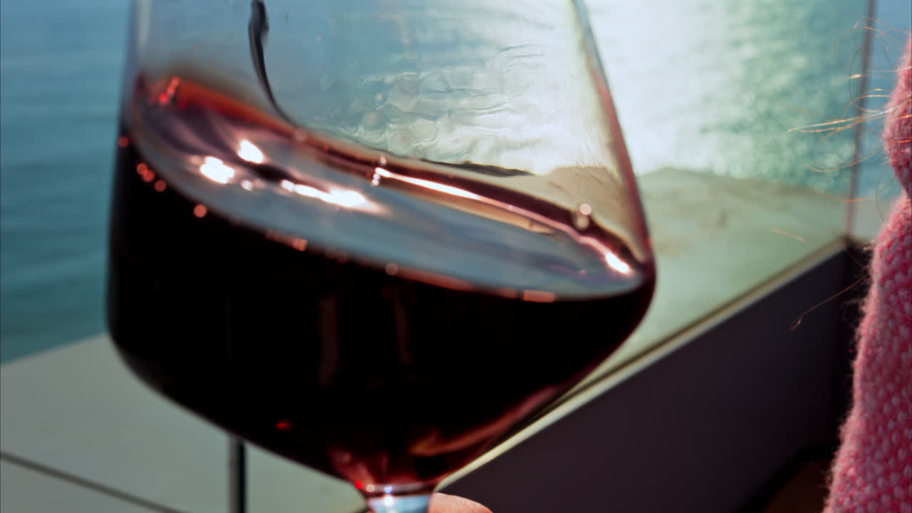 Close up of a woman swirling a glass of red wine on a table at a terrace with a sea view