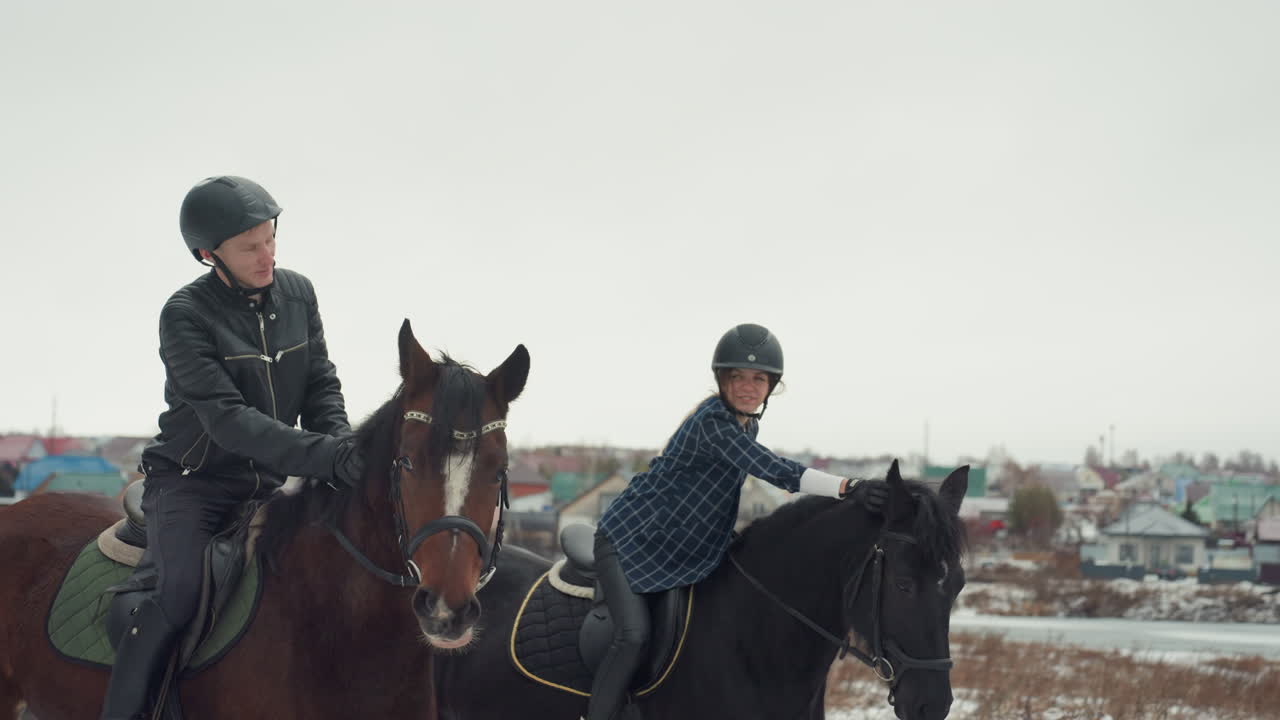 Due cavalieri caucasici che si esercitano vicino al villaggio, esercizio di addestramento in tandem con i partner che lavorano su ritmo ed equilibrio, galoppo e trotto su campo innevato, case all'orizzonte e lavoro di squadra focalizzato.