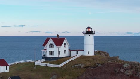 Tight-frame-of-quaint-lighthouse-atop-a-rocky-island-with-dusky-sky-and-a-soft-moon-over-the-Atlantic-ocean