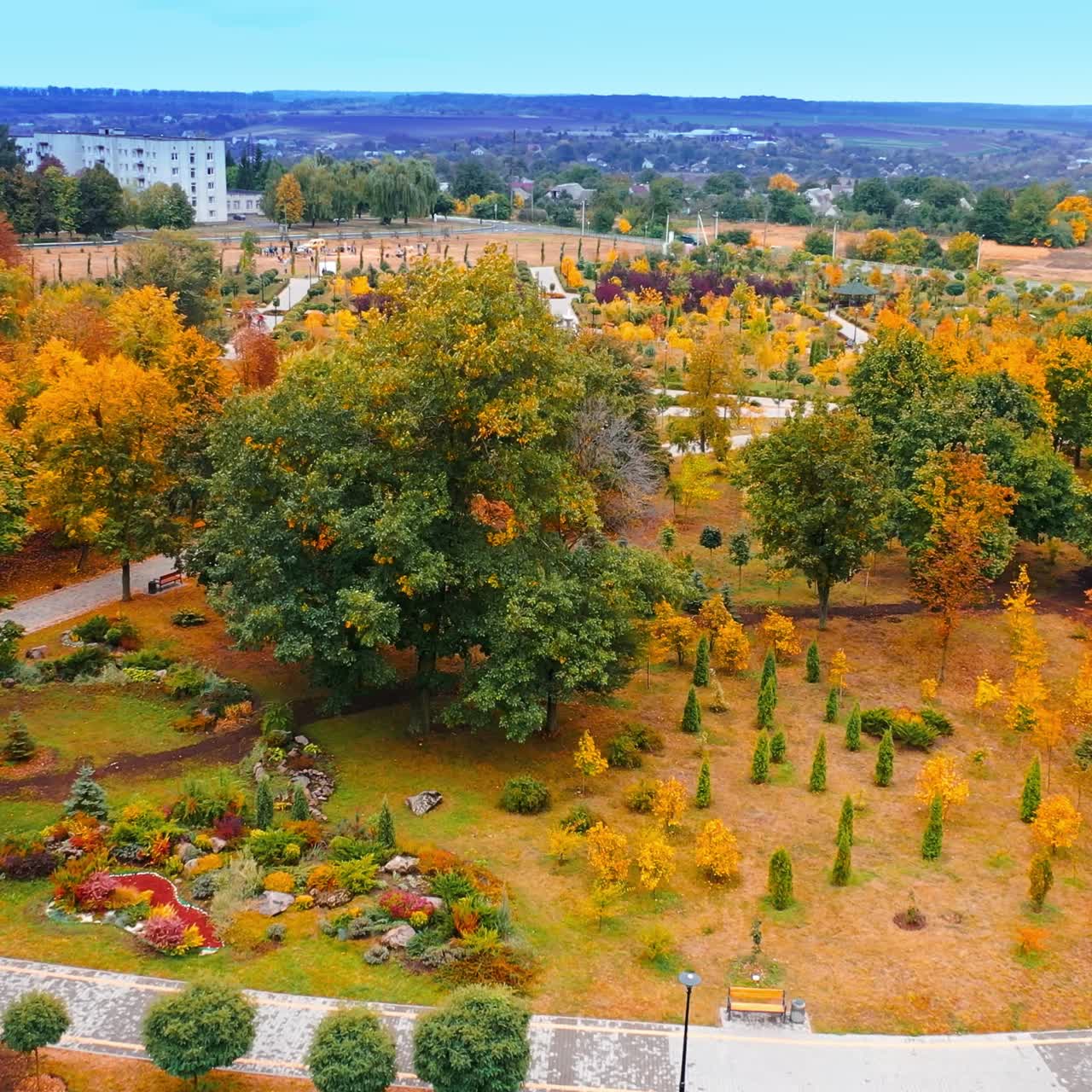 Green, yellow and orange colors of the trees and bushes in the man-made city park. Beautiful garden architecture in autumn season from air
