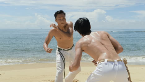 dos hombres bailando capoeira en la playa