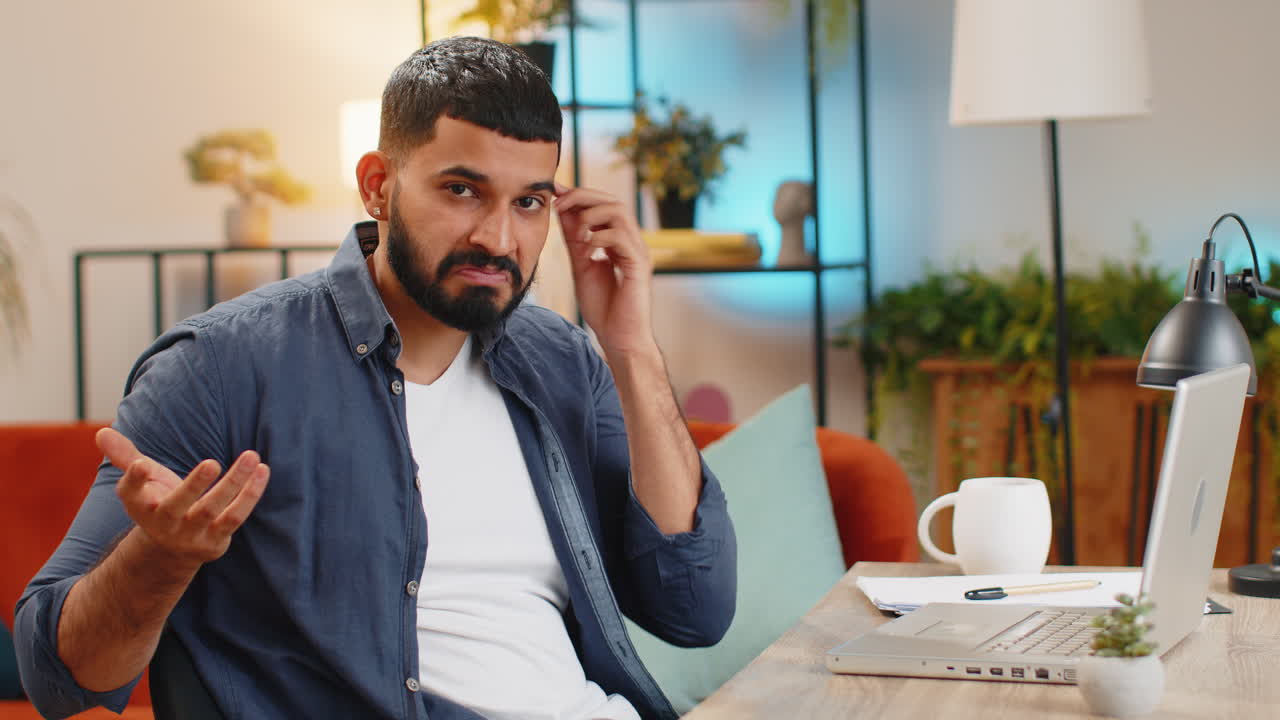 Confused Indian man working on laptop having doubts no answer idea being clueless at home office