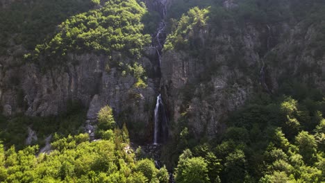 waterfall in the middle of rocky mountain slope revealed after green trees of forest in theth, albania