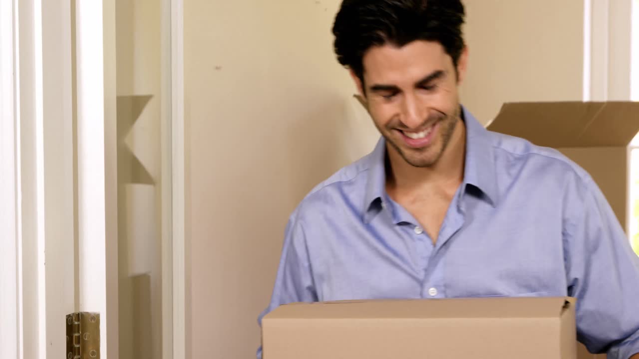 hombre sonriente llevando cajas en una casa nueva