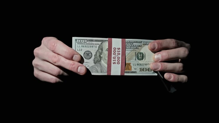 Pila di 10000 dollari americani in un fascio nelle mani di un uomo su sfondo nero.