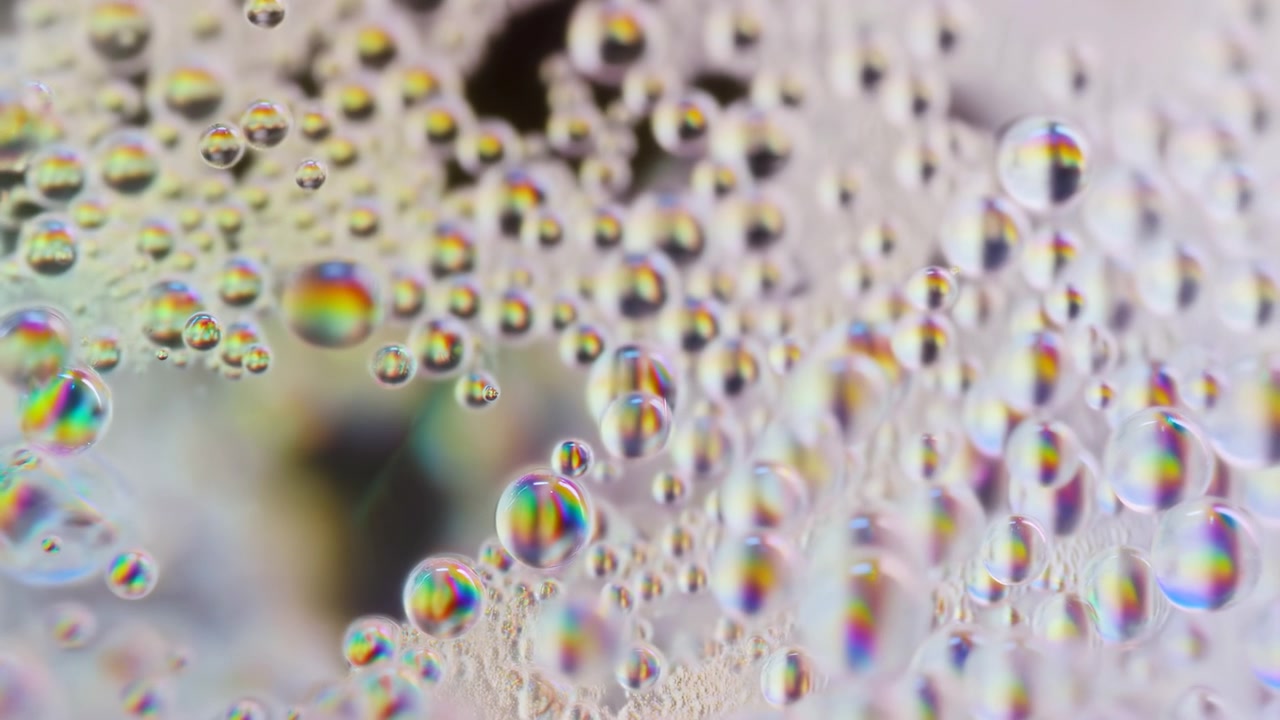 Molte bolle e goccioline trasparenti fluttuano su uno sfondo chiaro in una composizione astratta ravvicinata, con riflessi iridescenti dell'arcobaleno, texture liscia e lucida, sfocatura morbida, luce delicata e tonalità pastello rilassanti.