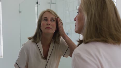 Mujer-Mayor-Caucásica-Mirando-En-El-Espejo-Del-Baño-Inspeccionando-Su-Rostro