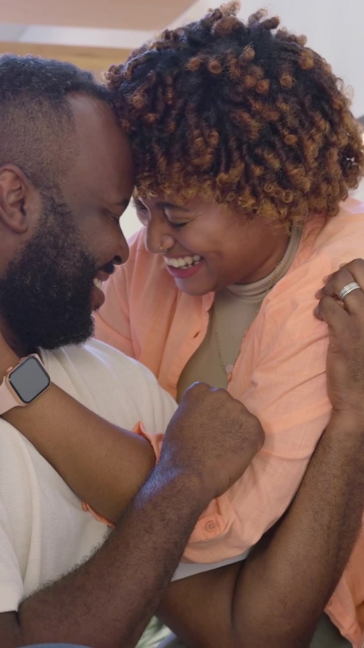 Vertical video: Wrapping arms behind, woman embracing man on couch, laughing, showing smartwatch