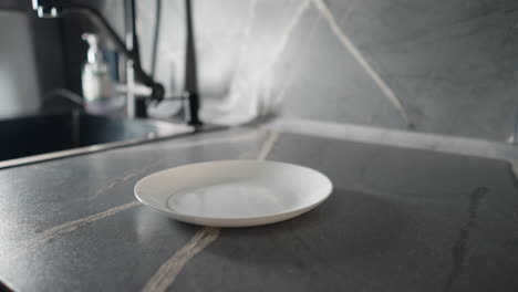 elderly woman in green sweatshirt placing food on empty white plate in modern kitchen. focus on hands and plate as part of her daily cooking and meal preparation routine