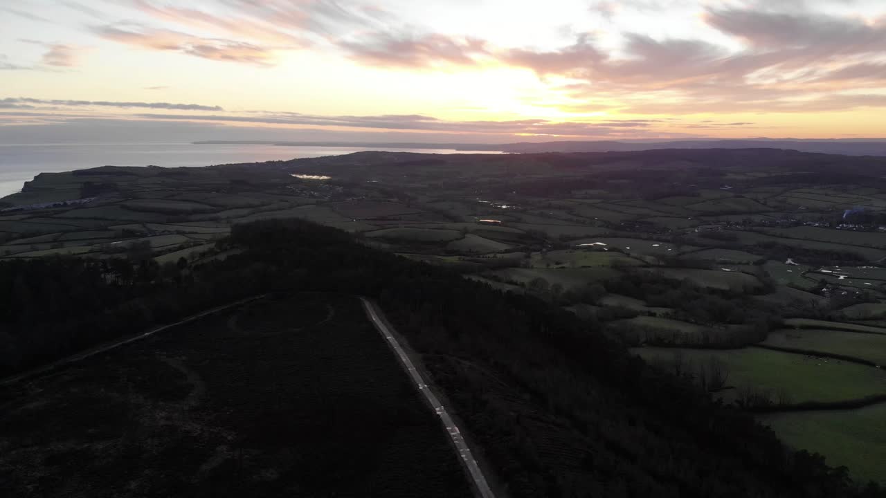 Sunset illuminating Mutters Moor and the surrounding countryside near Sidmouth, East Devon, aerial view at golden hour. pedestal down