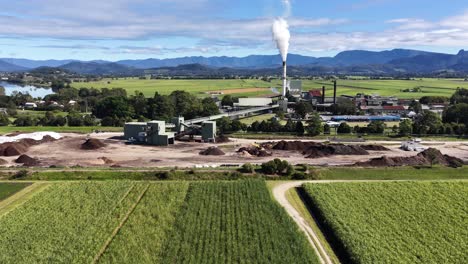drone footage captures a sugar mill surrounded by lush fields under clear skies in murwillumbah, nsw, australia