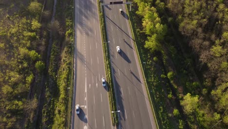 Aerial-View-Above-of-Busy-Highway-Road-during-daytime-surrounded-by-plush-green-vegetation-on-both-sides-and-a-small-canal-running-on-the-right-side